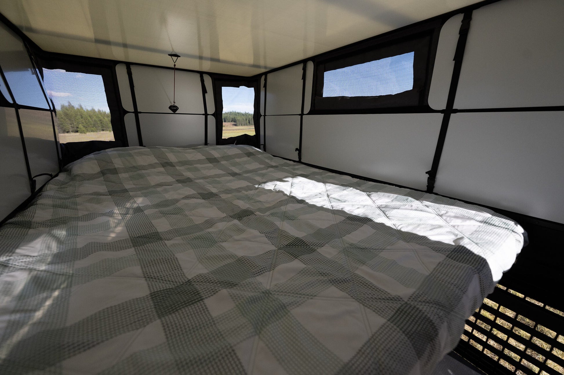 Queen bed made up inside the Oru Bruin truck camper, white wall panels either side and a lake through the panoramic windows