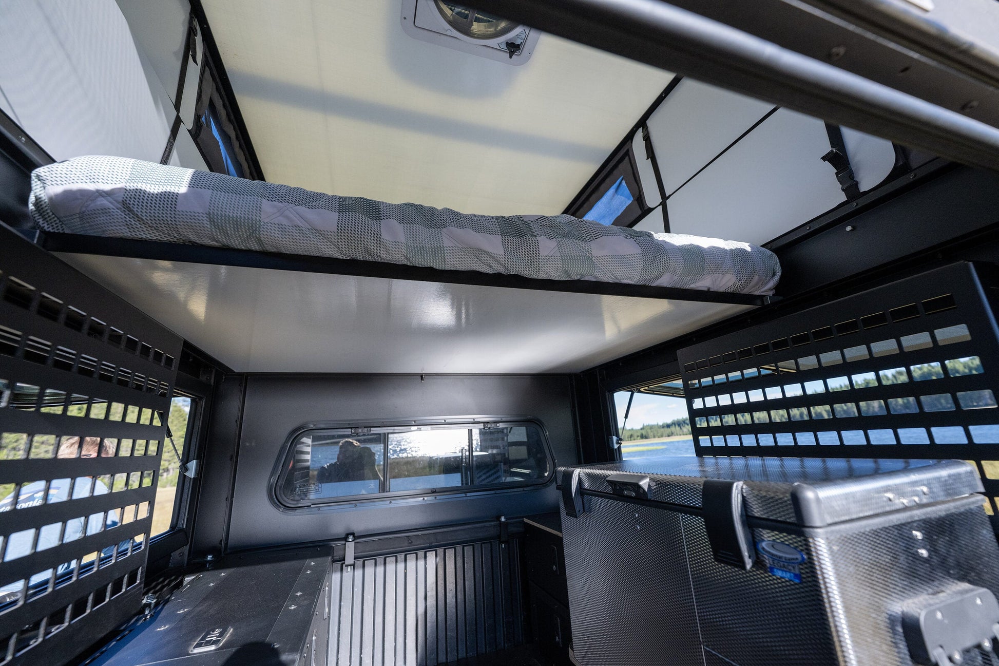 Oru Bruin camper interior with the bed platform stowed above the cabover, gear panels either side and a lake through the windows