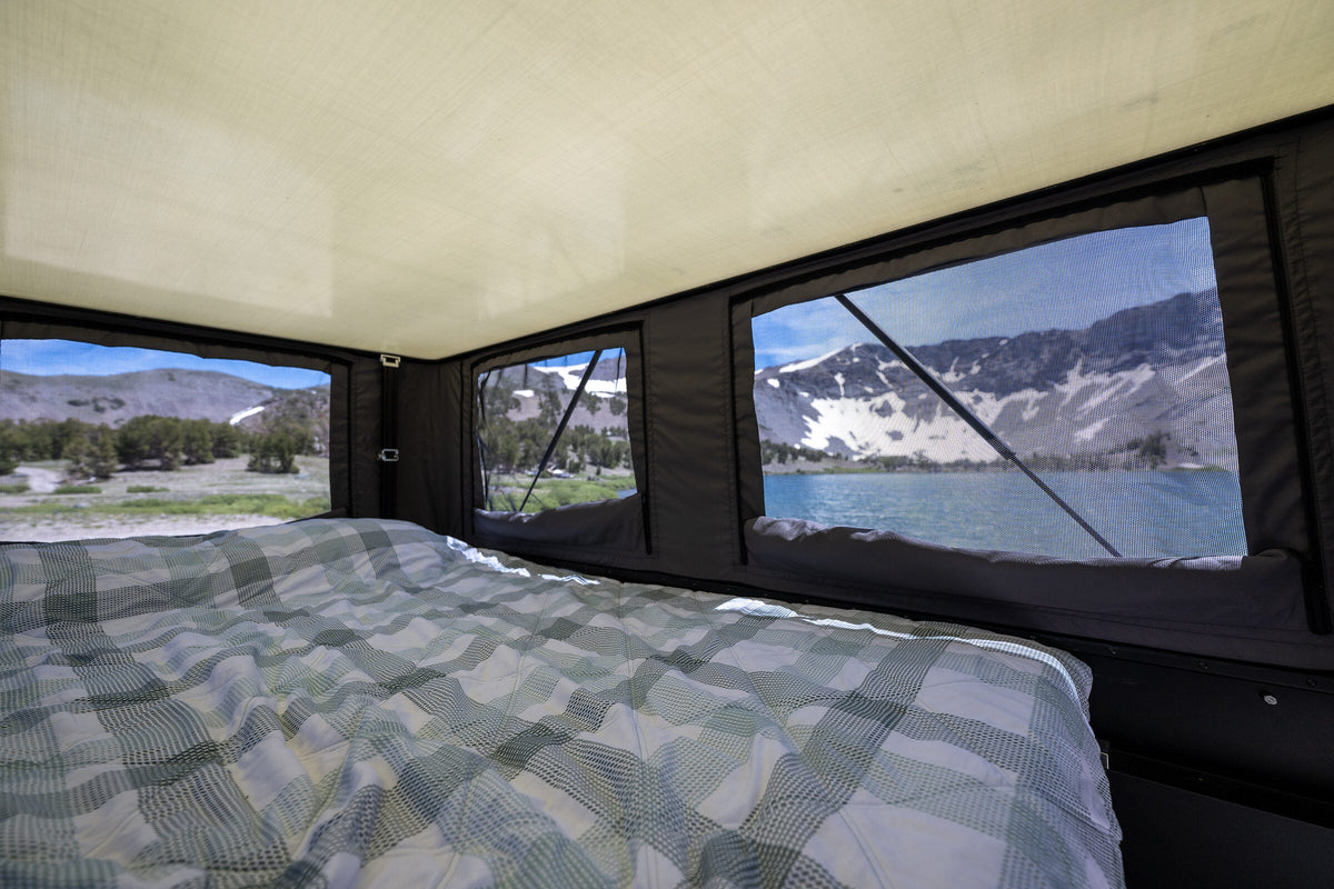 Queen bed inside the Oru Triton with an alpine lake and snow-covered ridge through the panoramic windows