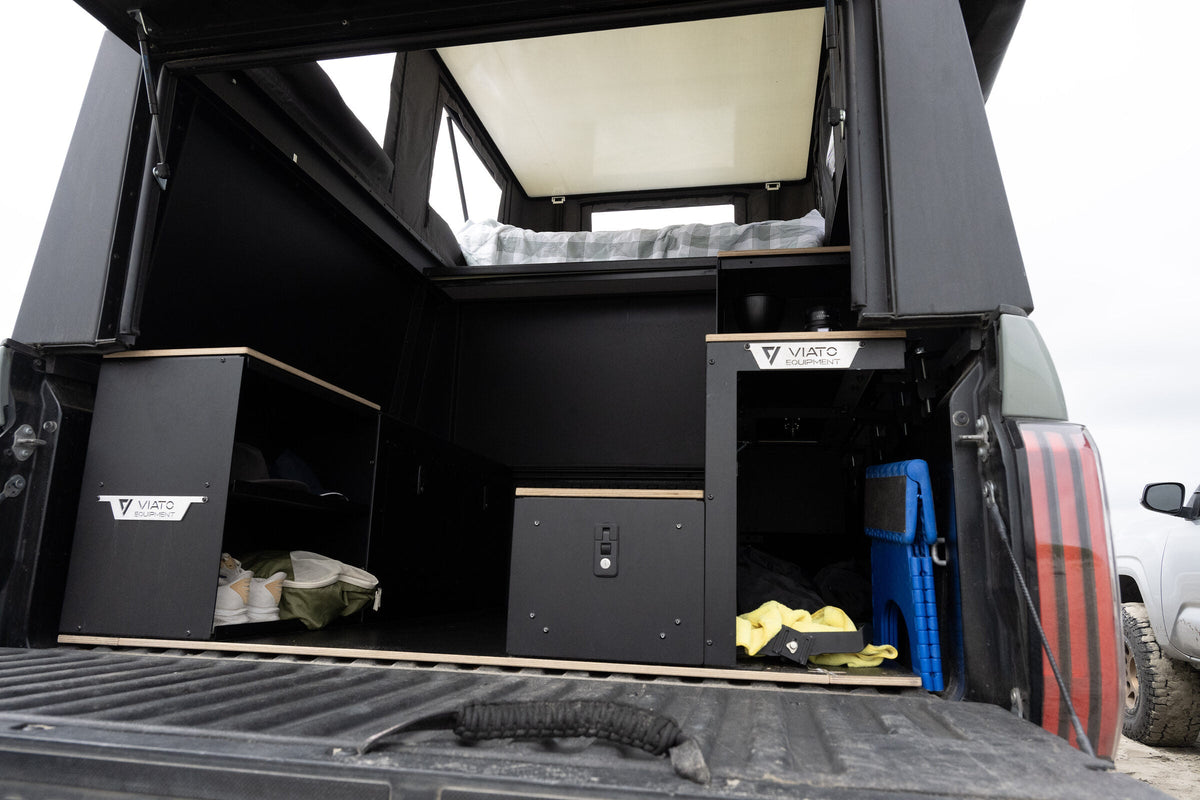 Oru Triton camper interior from the tailgate with the galley cabinets open and gear stowed on the bed floor