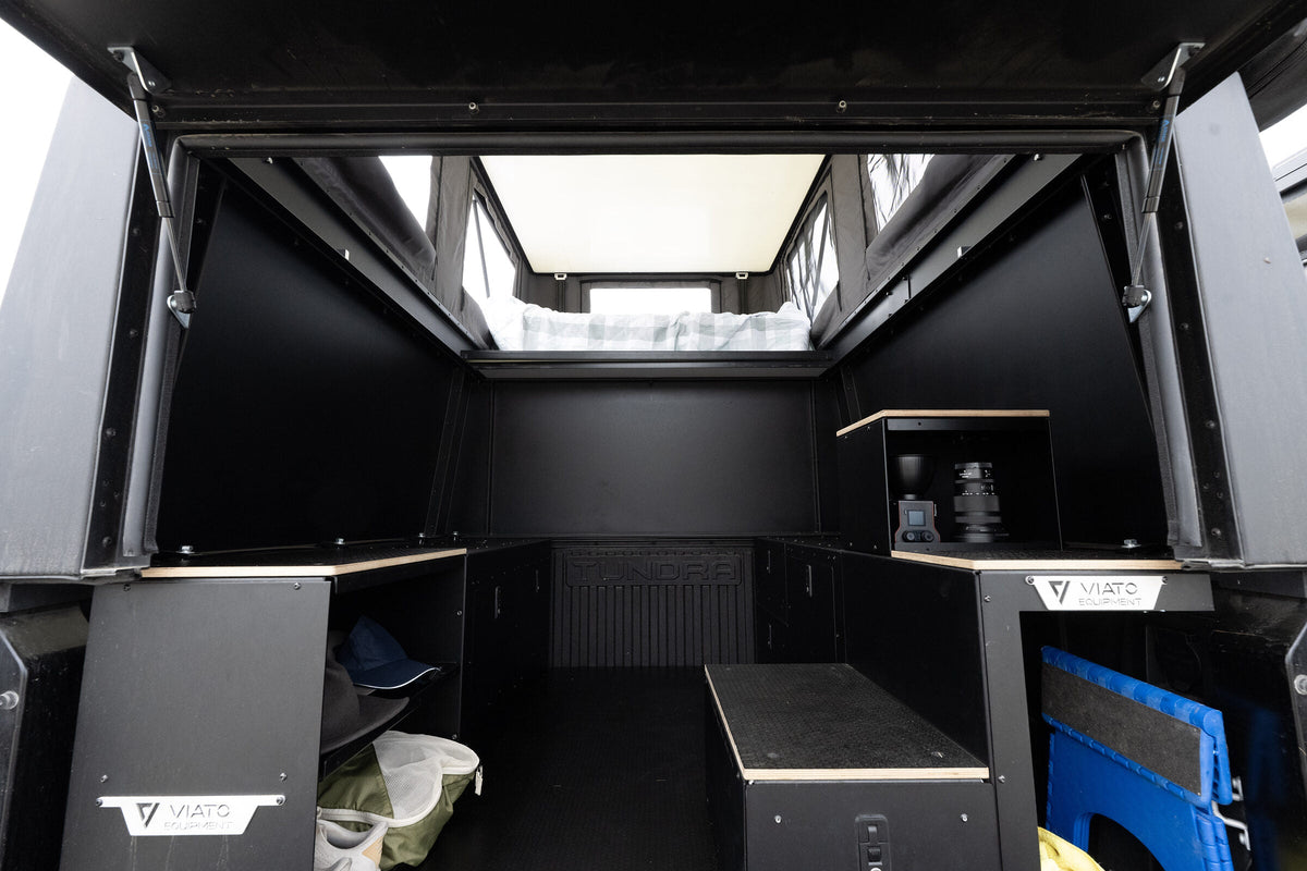 Inside the Oru Triton truck camper looking forward from the tailgate, bed platform overhead and the floor left clear