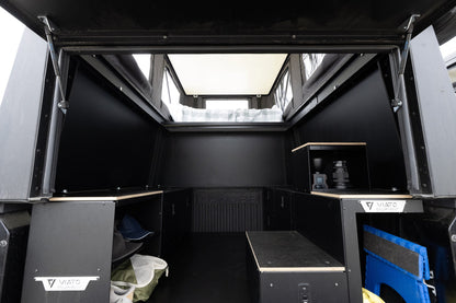 Inside the Oru Triton truck camper looking forward from the tailgate, bed platform overhead and the floor left clear