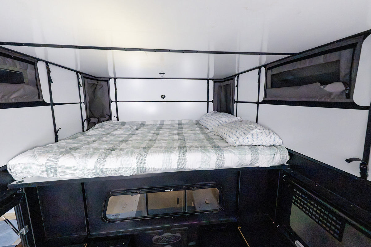 Queen bed made up inside the Oru Bruin XL, white wall panels either side and the tent windows open