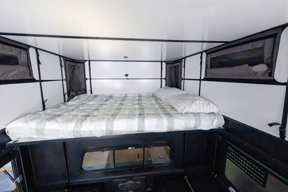 Queen bed made up inside the Oru Bruin XL, white wall panels either side and the tent windows open
