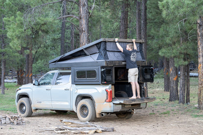Raising the roof on an Oru Bruin XL from the tailgate at a forest campsite