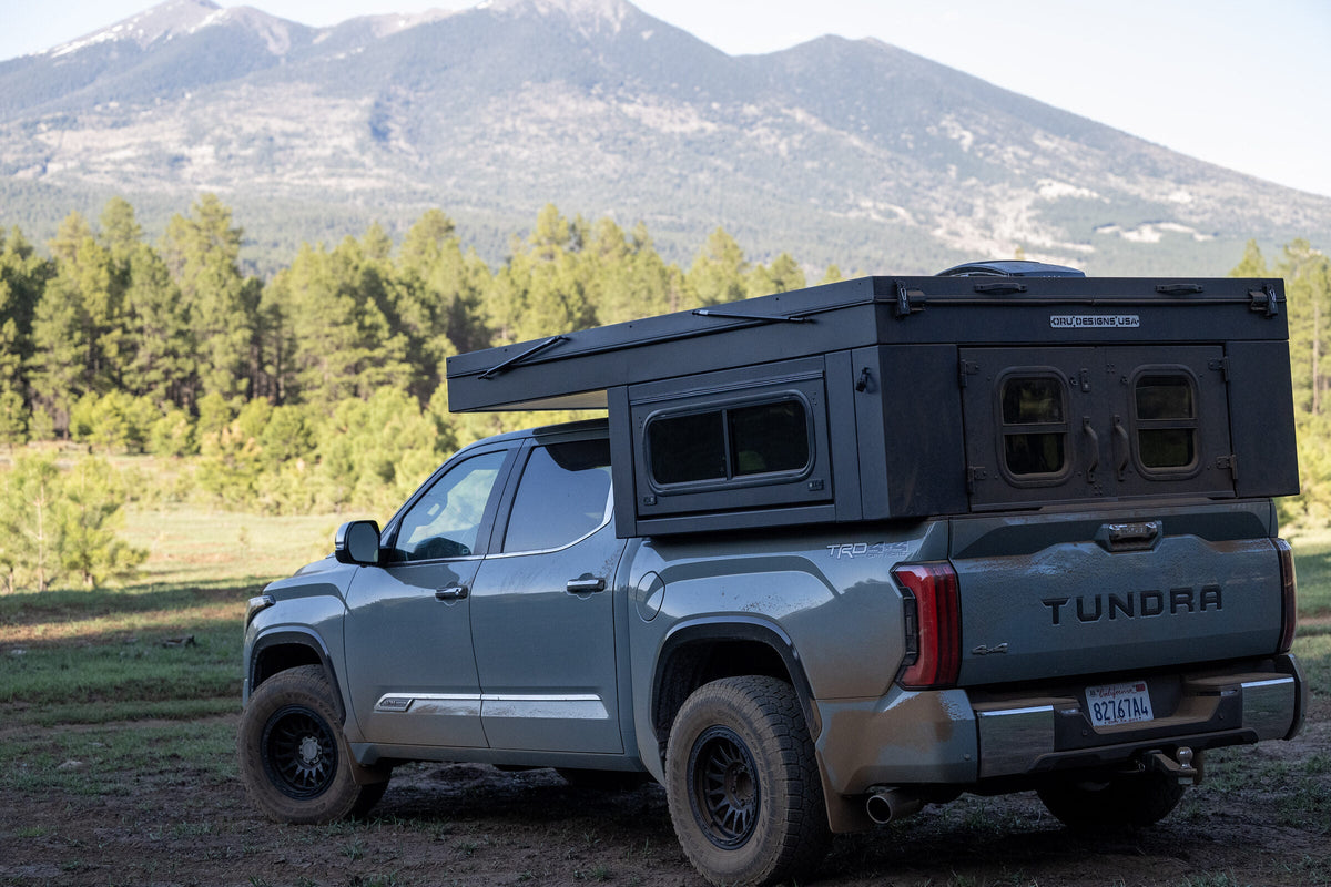 Oru Bruin XL with the roof down for travel, parked in a meadow below a mountain peak